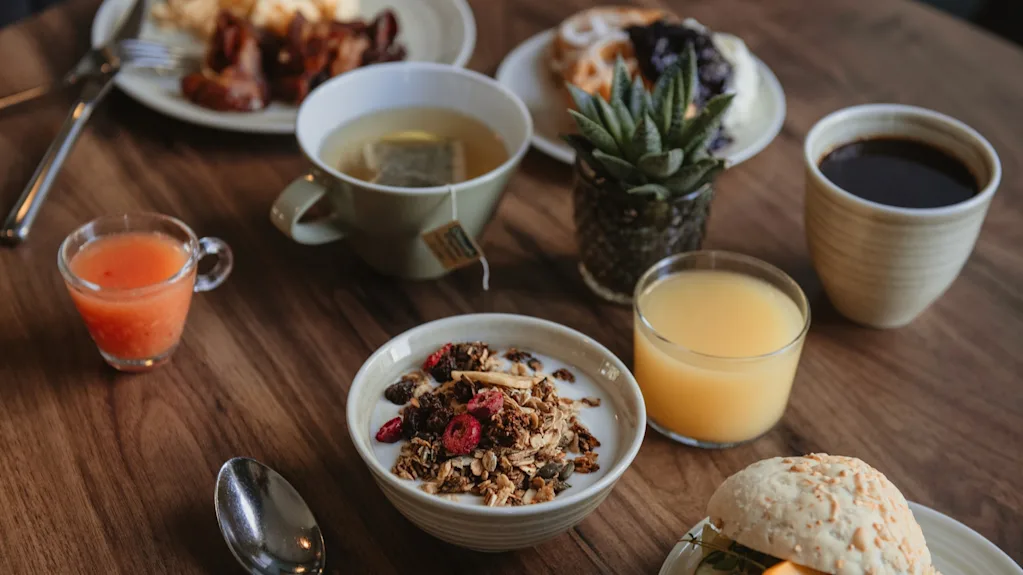 Home Hotel Post: En utsökt frukostbuffé på ett träbord med ägg, bacon, granola, juicer, kaffe och en smörgås.