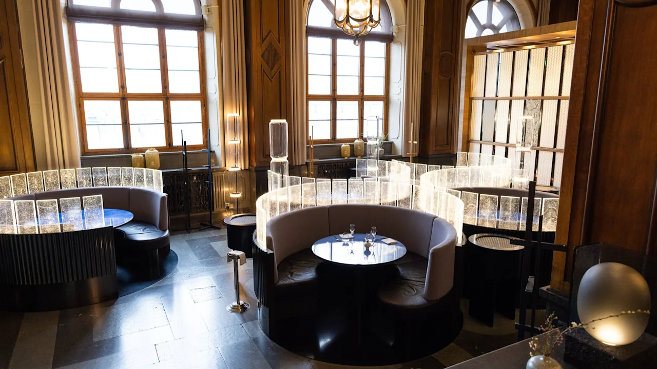 En elegant lounge på Clarion Hotel Post med buede sitteplasser, runde bord og opplyste skillevegger, som skaper en innbydende atmosfære.