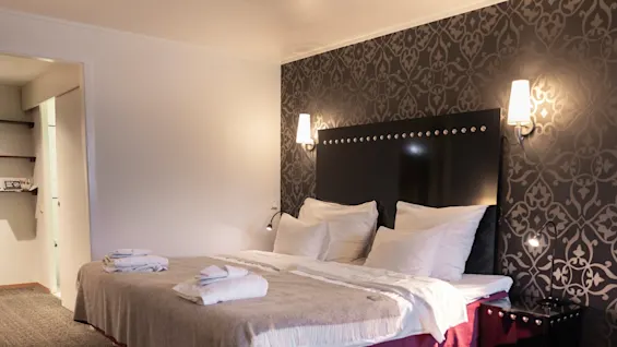 A cozy hotel room with a large bed, patterned wallpaper, and soft lighting, ready for a comfortable stay.