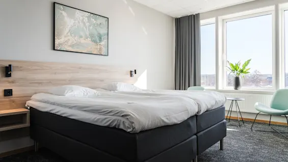 Ett ljust och inbjudande hotellrum med två bekväma sängar, ett stort fönster med naturskön utsikt och en mysig sittgrupp.