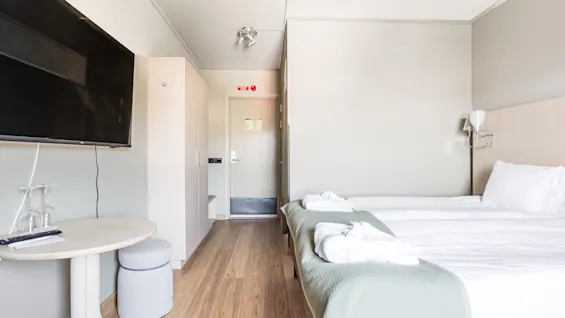 A bright and modern hotel room with a comfortable bed, a wall-mounted TV, and a small table.
