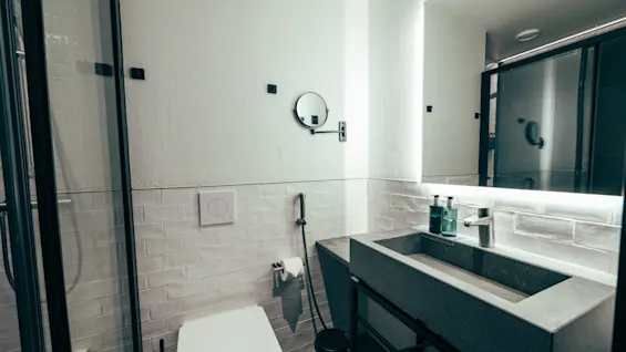 A modern bathroom with a sleek concrete sink, a large illuminated mirror, a toilet, and a glass-enclosed shower.