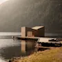 Moderni puinen saunarakennus laiturin päässä tyynen järven rannalla metsäisen vuoren siimeksessä.