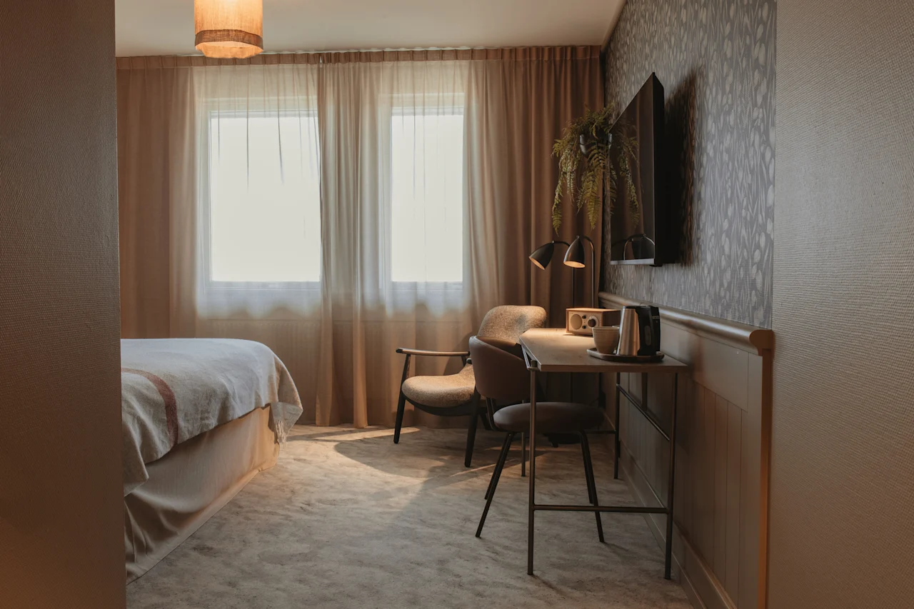 Et hyggeligt hotelværelse med en komfortabel seng, et funktionelt arbejdsområde og varm belysning, perfekt til afslapning eller produktivitet.