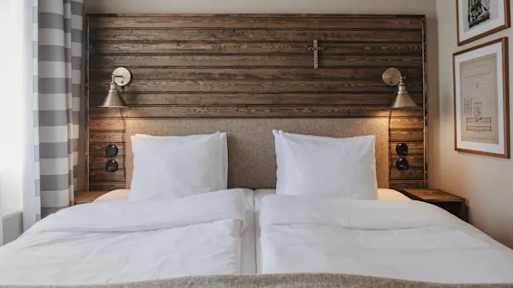 A cozy hotel room with a large bed, wooden headboard, and warm lighting, inviting relaxation.