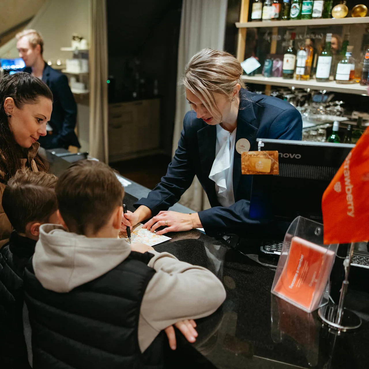 Hotellin vastaanottovirkailija auttaa perhettä kartan kanssa aulassa.