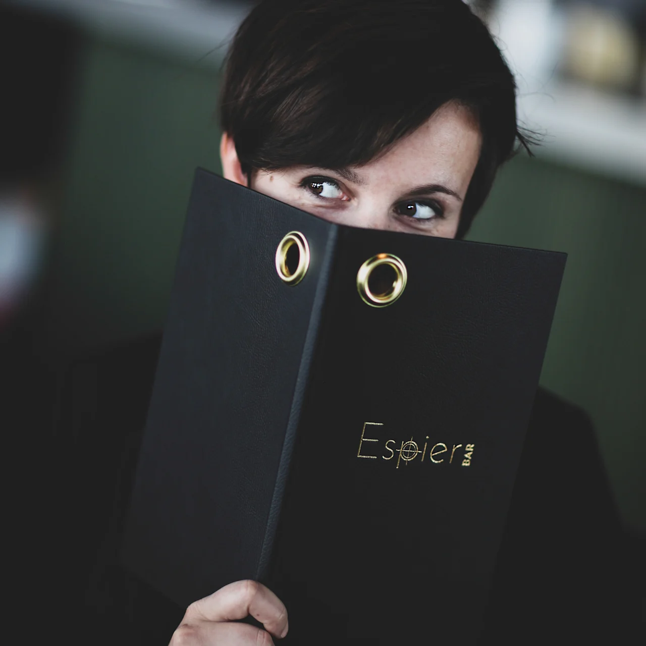 En person kikar över en svart meny eller pärm med texten Espier BAR, tittar åt sidan.