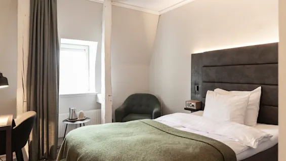 Viihtyisä hotellihuone Home Hotel Victoriassa, jossa on mukava sänky, vihreä peitto, ikkuna ja pieni oleskelutila.