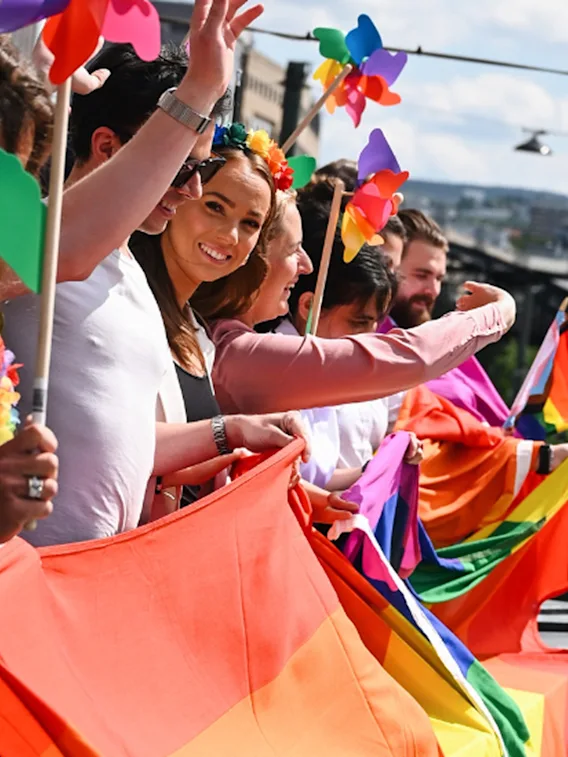 En gruppe mennesker som står på en balkong og vifter med Pride-flagg
