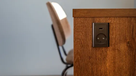 En treplate med en stikkontakt og USB-port er installert. En uklar stol er synlig i bakgrunnen mot en nøytral vegg.