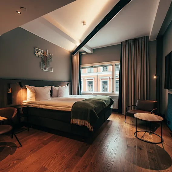 Viihtyisä ja moderni hotellihuone, jossa on parivuode, puulattia ja lämmin valaistus.