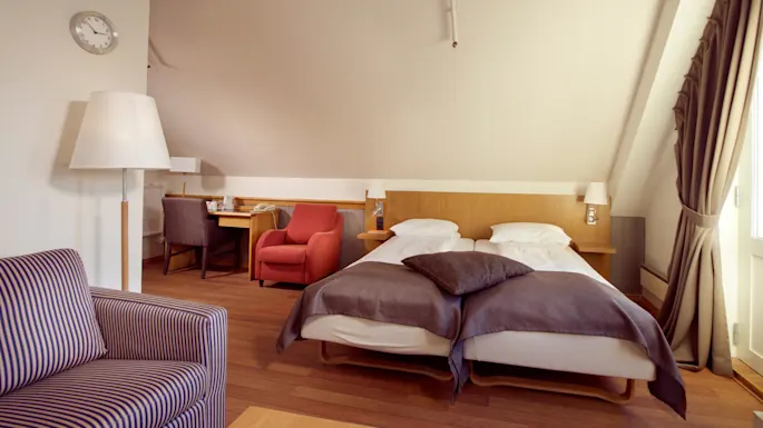 A neatly arranged hotel room with twin beds, furniture, and warm lighting.