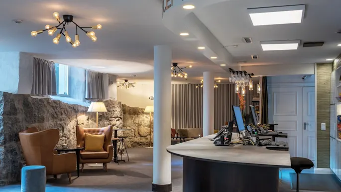 Et moderne resepsjonsområde med komfortable sitteplasser, stilig belysning, datamaskiner på disken og steinvegger som skaper en innbydende atmosfære.