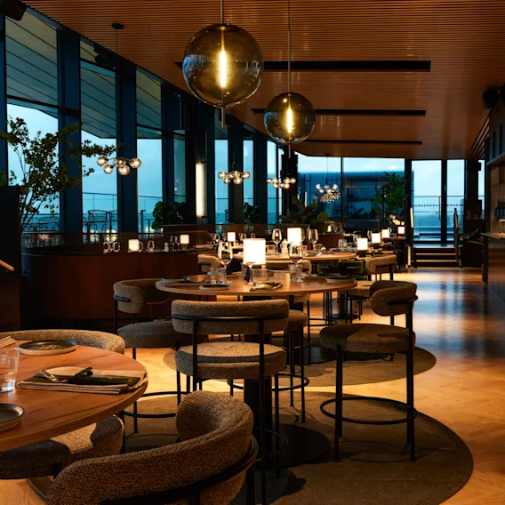 Ravintola NOR Clarion Hotel Helsinki Airportissa, tyylikäs tila kutsuvilla pöydillä, lämpimällä valaistuksella ja suurilla ikkunoilla.