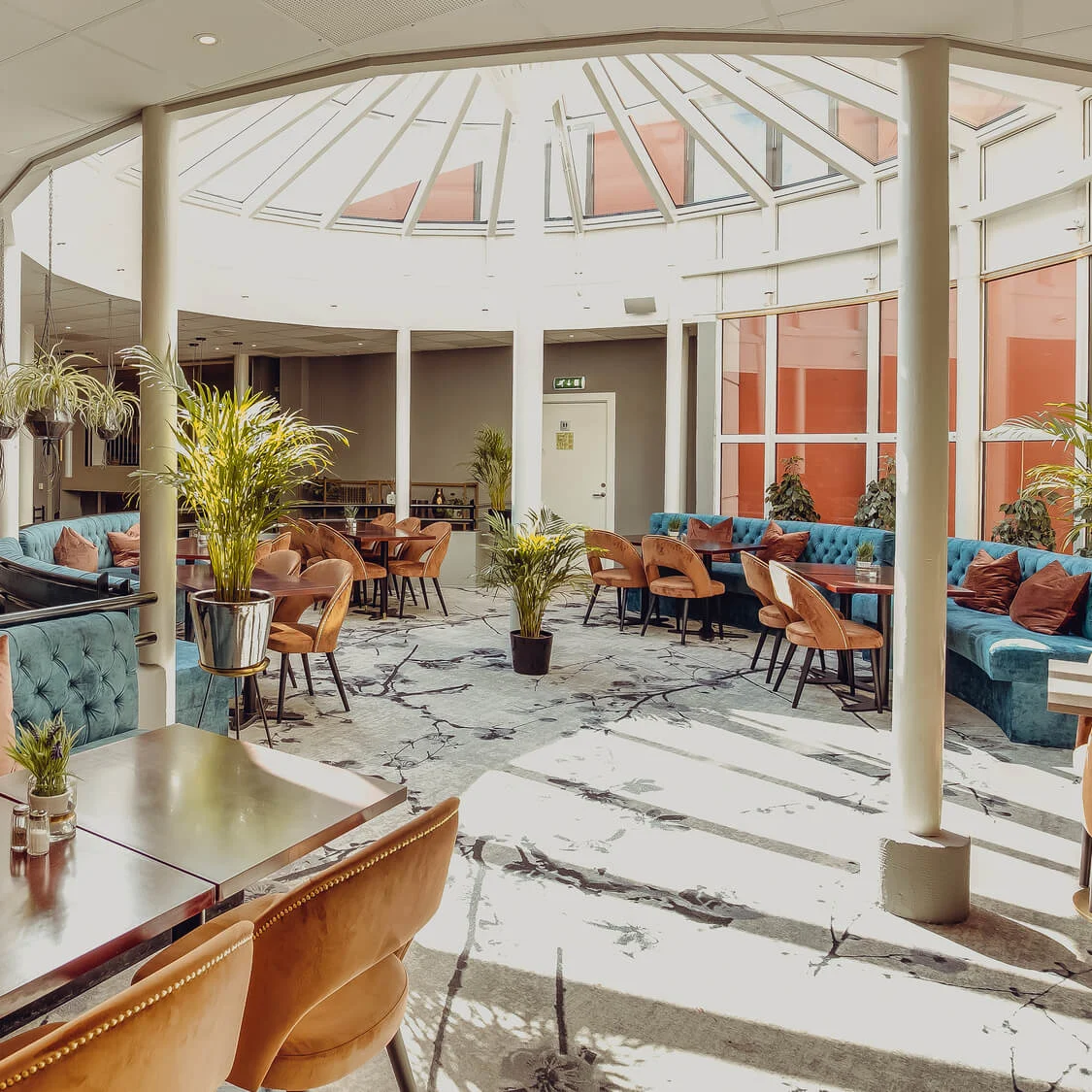 An elegant lounge with plush seating and potted plants under a sunlit atrium.