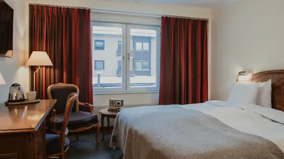 Ett bekvämt hotellrum med en säng, ett skrivbord och ett fönster som visar en snöig utomhusvy.