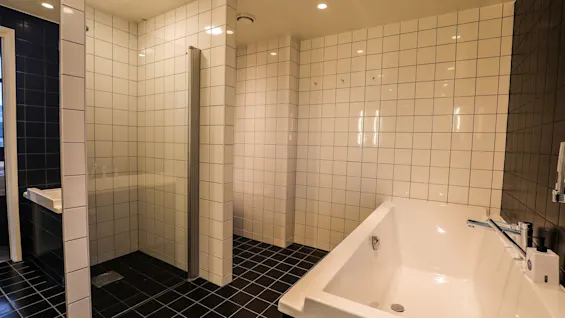 Et hvitt badekar står i et flislagt bad med svart og hvit kontrast. Rommet har også et dusjområde med en glassvegg.