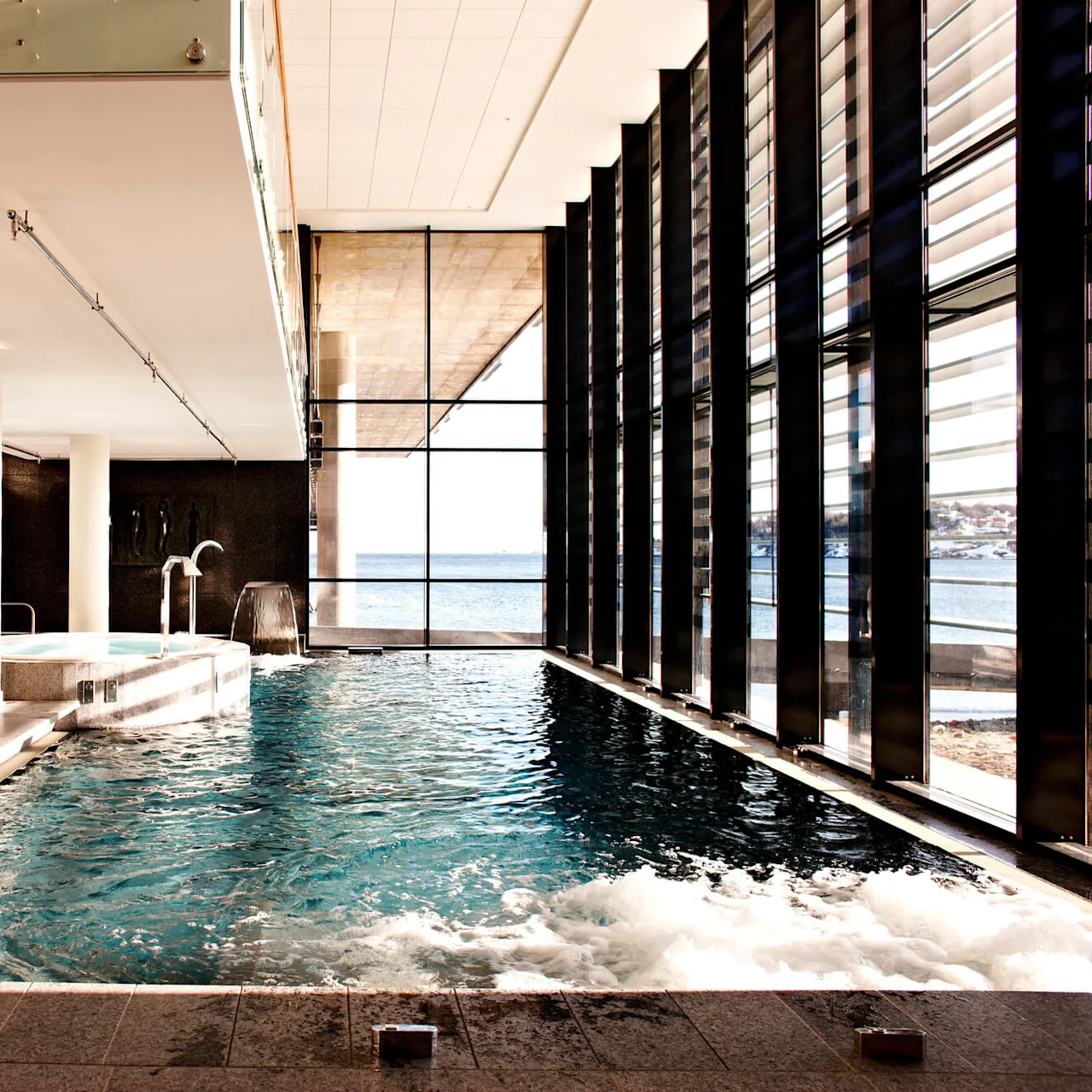 Indendørs pool med rolige vand og moderne arkitektur, med udsigt over et stille hav gennem store vinduer.