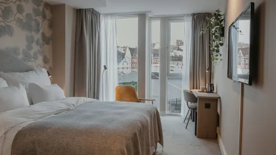 Et moderne hotelværelse med en komfortabel seng, et skrivebord og et stort vindue med udsigt over en by og vand.