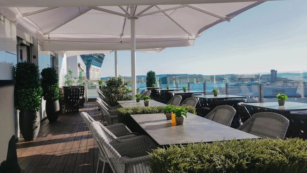 An inviting outdoor terrace with dining tables and chairs under umbrellas, offering a scenic view of the water and city.