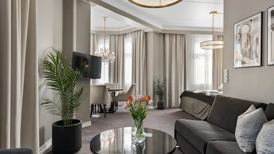 En moderne hotelsuite med en komfortabel sofa, spisebord og en seng, med stilfuld indretning og friske blomster.