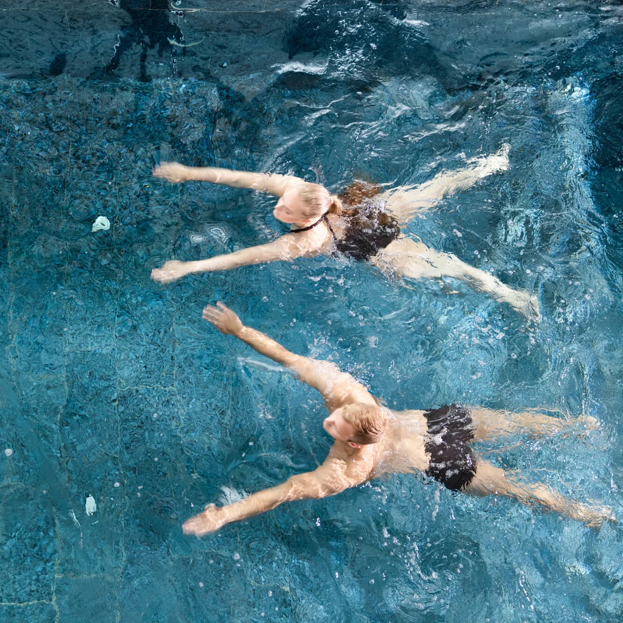 To personer svømmer under vandet i en klar blå swimmingpool.