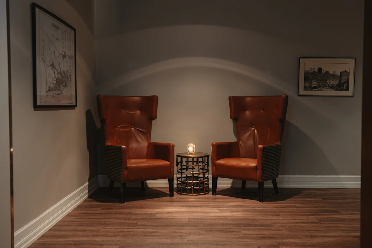 En mysig sittgrupp på Home Hotel Grand, Helsingborg, med två bruna fåtöljer och ett ljusupplyst bord, perfekt för avkoppling.