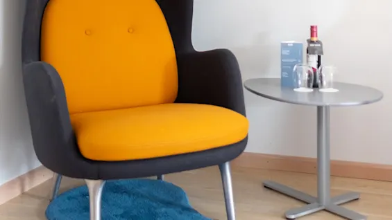 Orange stol står bredvid ett grått bord med flaskor och glas på ett trägolv mot en vit vägg.