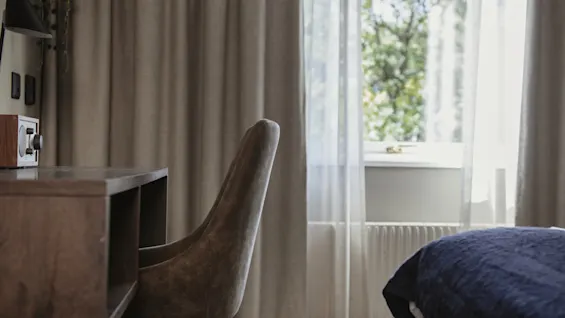 Ett bekvämt hotellrum med ett skrivbord, stol och ett fönster med skira gardiner som erbjuder utsikt över frodig grönska.