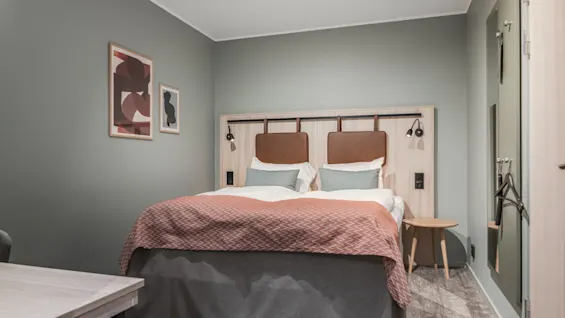 Et moderne hotellrom med en komfortabel seng, nattbord og kunst på veggen, klart for et avslappende opphold.