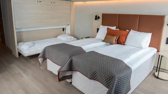 Et moderne hotellrom med to komfortable senger og en ekstra nedfellbar seng, som tilbyr fleksible sovemuligheter.