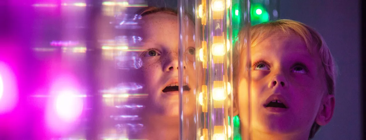 Kid looking at a glas wall filled with colors. 