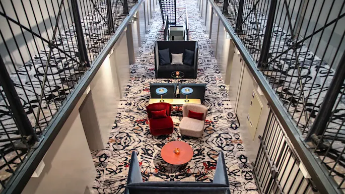 En hevet gangvei med stoler og bord, symmetrisk arrangert, med et mønstret teppe; moderne interiørdesign.