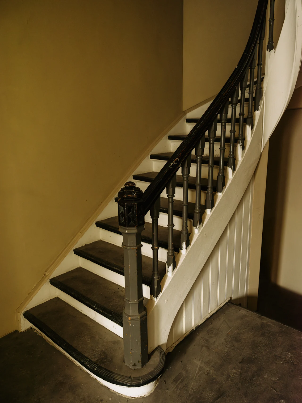 En elegant, buet trappe med mørke trætrin og gelænder, samt hvide stødtrin, der fører opad i en gammel bygning.