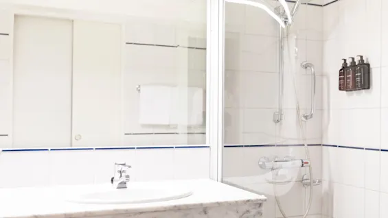 Puhdas ja moderni kylpyhuone, jossa on pesuallas marmoritasolla, suuri peili ja suihku lasiovilla ja seinään kiinnitetyillä annostelijoilla.