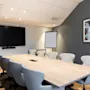 A modern meeting room with a large screen, a wooden table, and comfortable chairs, ready for presentations and discussions.