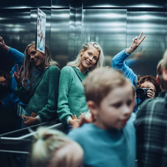 People smiling and taking photos in a reflective elevator, enjoying a moment together.