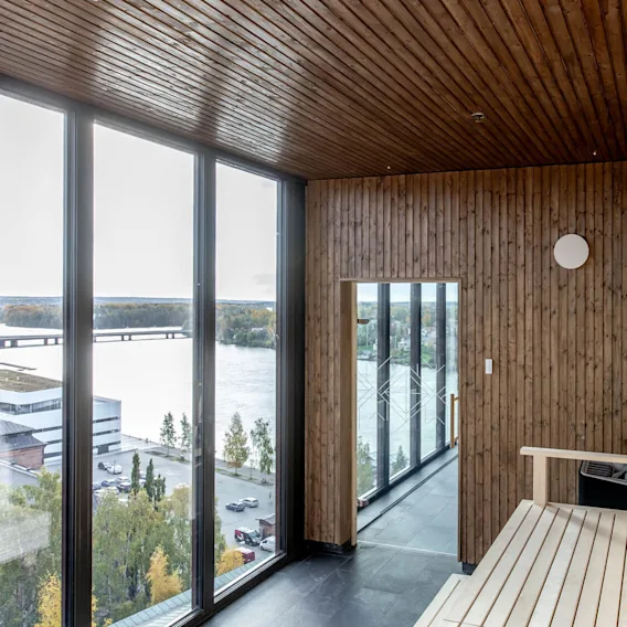 Ett träklätt basturum med stora fönster erbjuder en naturskön utsikt över en flod och bro, vilket ger en fridfull miljö ovanför en livlig stadsbild.