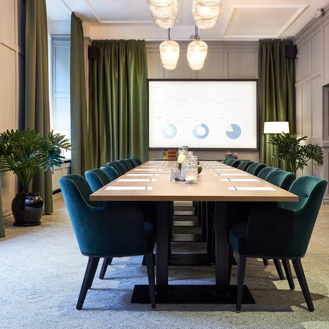 A conference room with a long table set for a meeting, a projector screen displaying charts in the background.