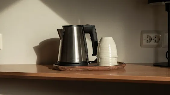 En silverfärgad vattenkokare och två staplade vita koppar på en träbricka, redo för en varm dryck.