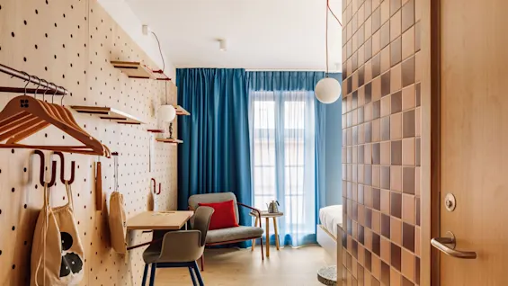A modern and inviting hotel room at hobo oslo, showcasing a versatile pegboard wall, work area, and bright blue curtains.