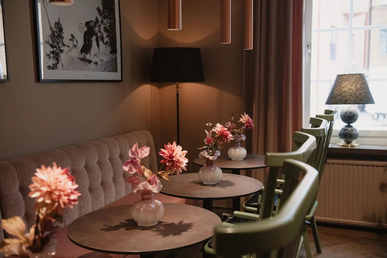 Et koselig kafé- eller loungeområde med små bord, sitteplasser og blomster, opplyst av myk belysning.
