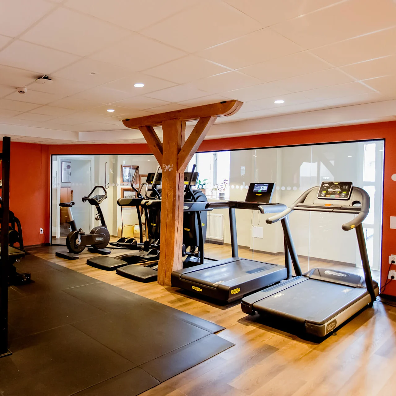 Exercise equipment in a gym with treadmills, weights, and a stationary bike, set against orange walls and wood accents.
