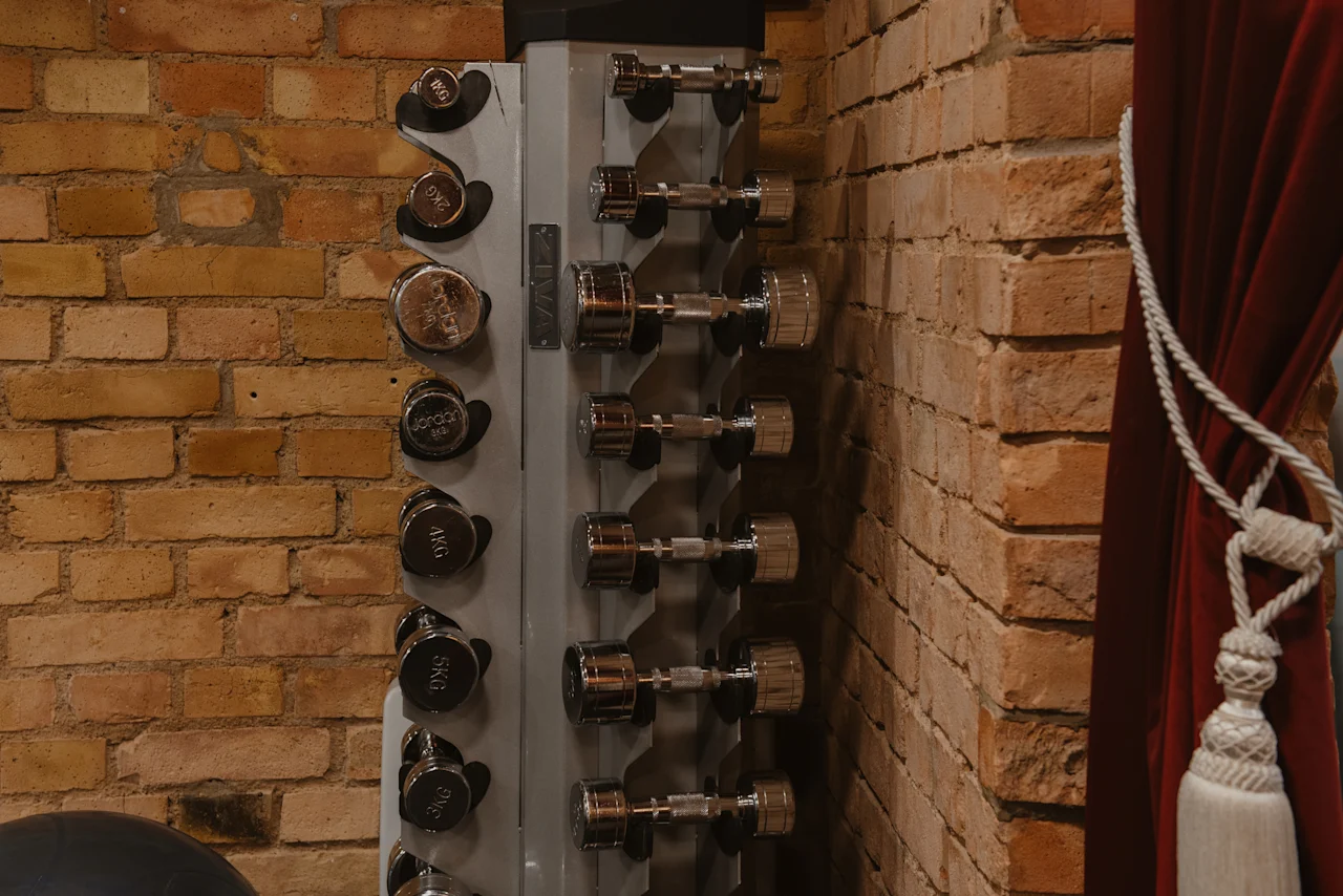 Hantelställ med vikter från 1KG till 5KG i ett gymområde på Home Hotel Grand, Helsingborg, bredvid en tegelvägg och röd gardin.