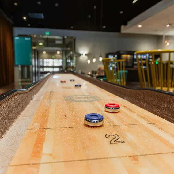 Ett shuffleboard-spel med röda och blå puckar och siffran 2 på bordet, placerat i en modern och inbjudande lounge.