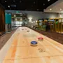 A shuffleboard game with red and blue pucks and the number 2 on the table, set in a modern and inviting lounge.