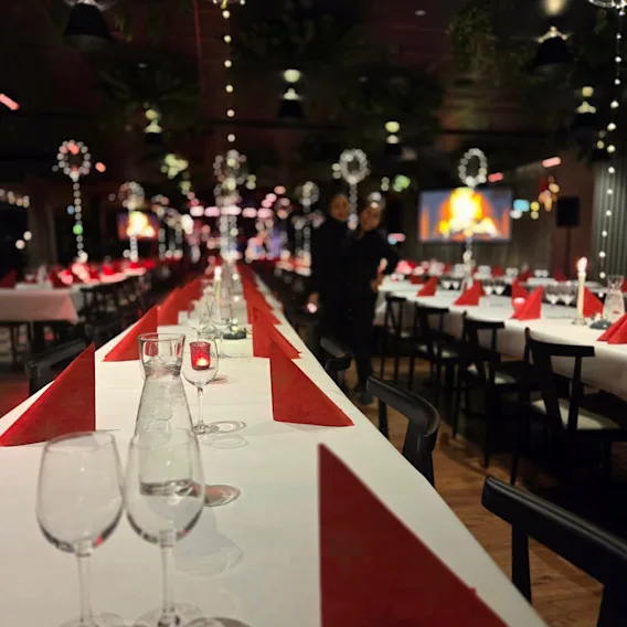 Långbord dukade med vita dukar och röda servietter inför en julfest.