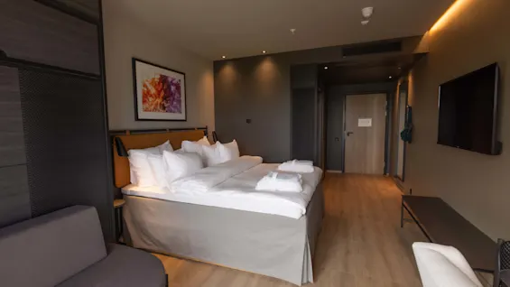 Ett välarrangerat hotellrum med en stor säng, väggmonterad TV och inramad konst som ger en modern och bekväm stämning.