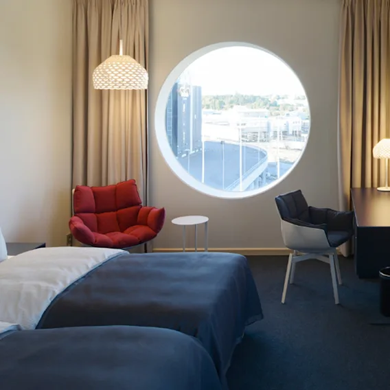 Ett modernt hotellrum med två sängar, ett skrivbord och unika runda fönster som erbjuder utsikt.