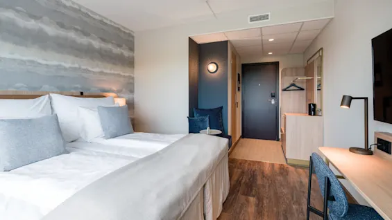 Et lyst og moderne hotellrom med en stor seng, en dedikert arbeidsplass og en koselig sitteplass.